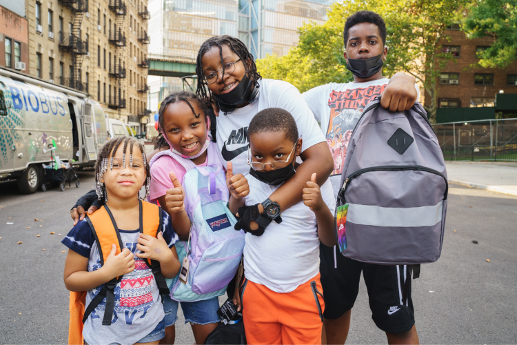 Back-to-school Supply Drive - Group of diverse children with backpacks giving thumbs up