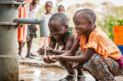 Children joyfully drinking clean water from a well - showing the happiness that clean water brings