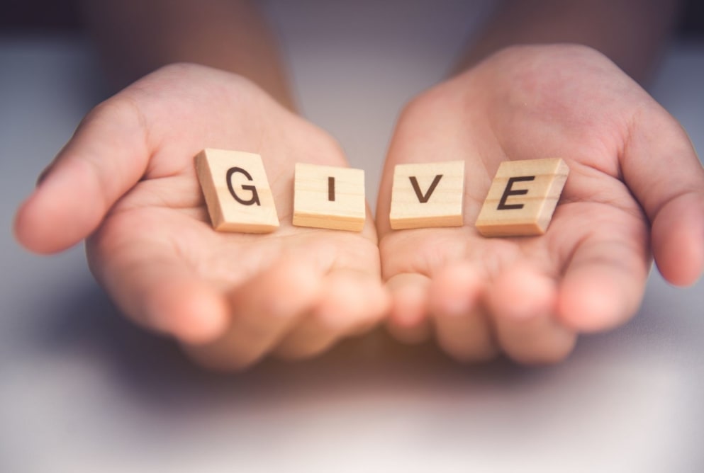 Hands holding GIVE blocks representing charitable support and hope restoration