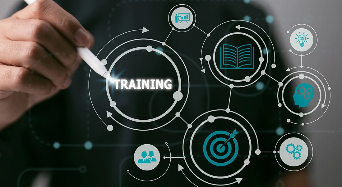 Hand pointing to digital training interface with interconnected learning icons including books, lightbulbs, gears, and collaboration symbols